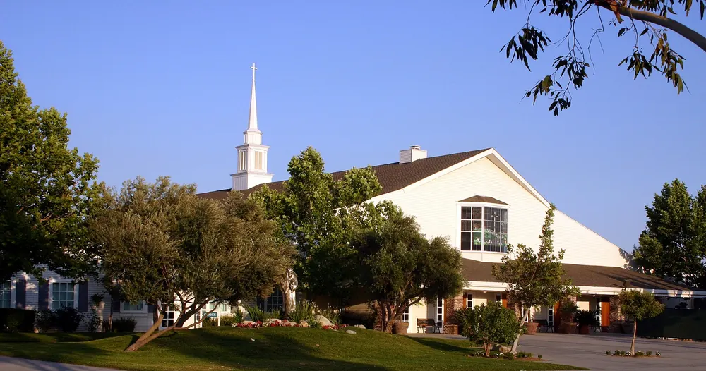 White church with a tall steeple among oak trees under a clear sky