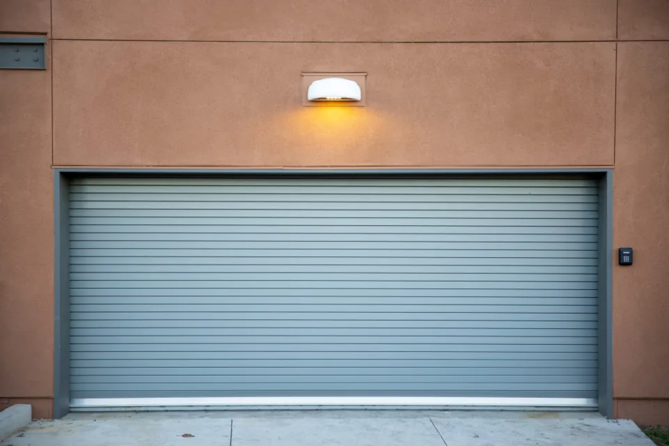a closed roll-up door in a stucco wall under a wall light